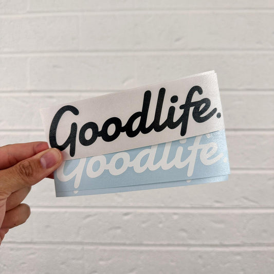 Hand holding a 'Goodlife' branded vinyl sticker against a light gray background
