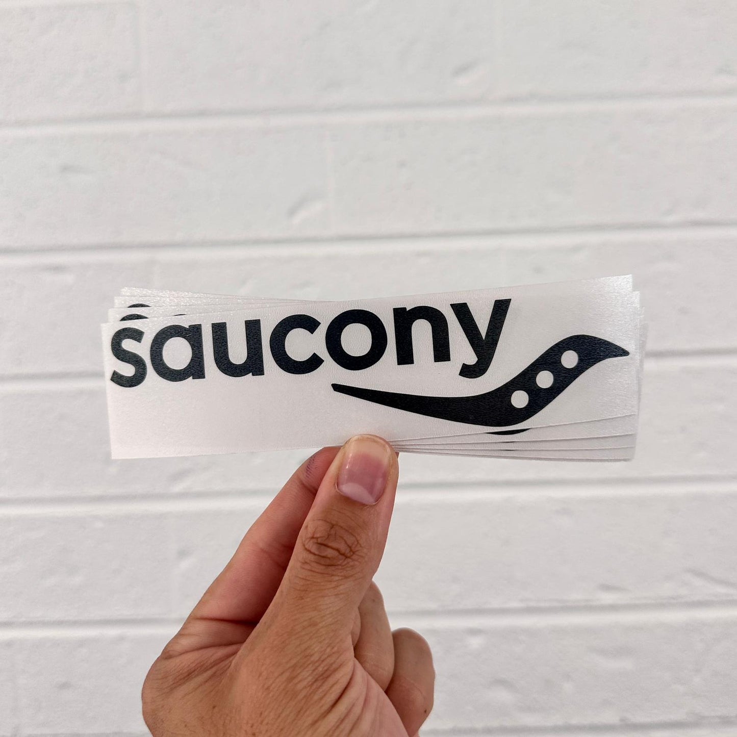 Hand holding a Saucony vinyl sticker against a light gray background
