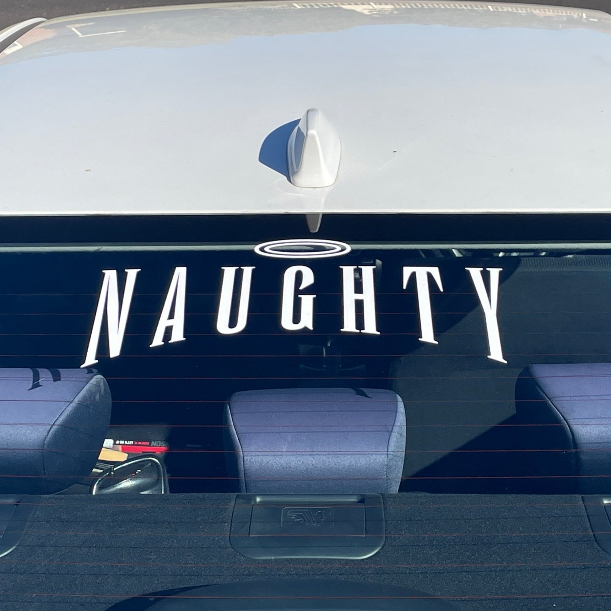 Vinyl decal on the rear window of a car with the word 'Naughty' in bold white letters and a halo above the letter 'A