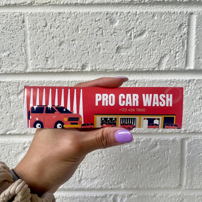 Hand holding 'Pro Car Wash' bumper sticker with illustration of a car wash and contact number