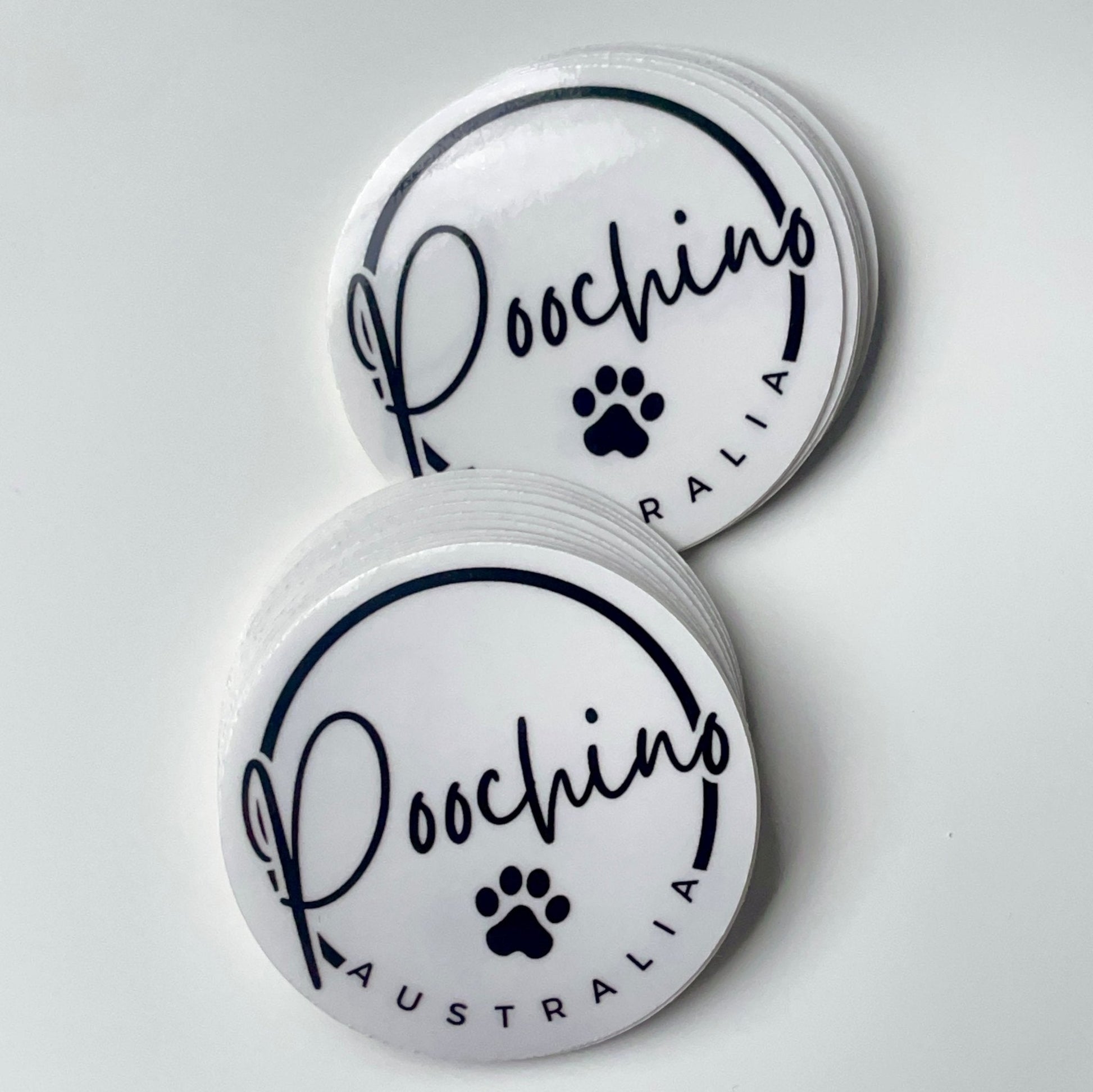 Stacks of round white 'Poochino Australia' stickers with a paw print logo.