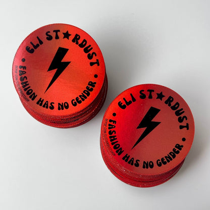 Stacks of round red 'Eli Stardust' stickers with a black lightning bolt and 'Fashion Has No Gender' text.