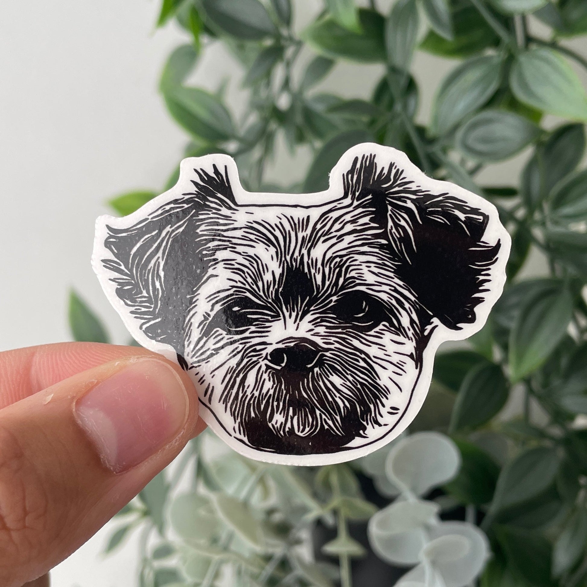 Die cut sticker featuring a detailed black and white illustration of a dog's face, held in front of green leaves