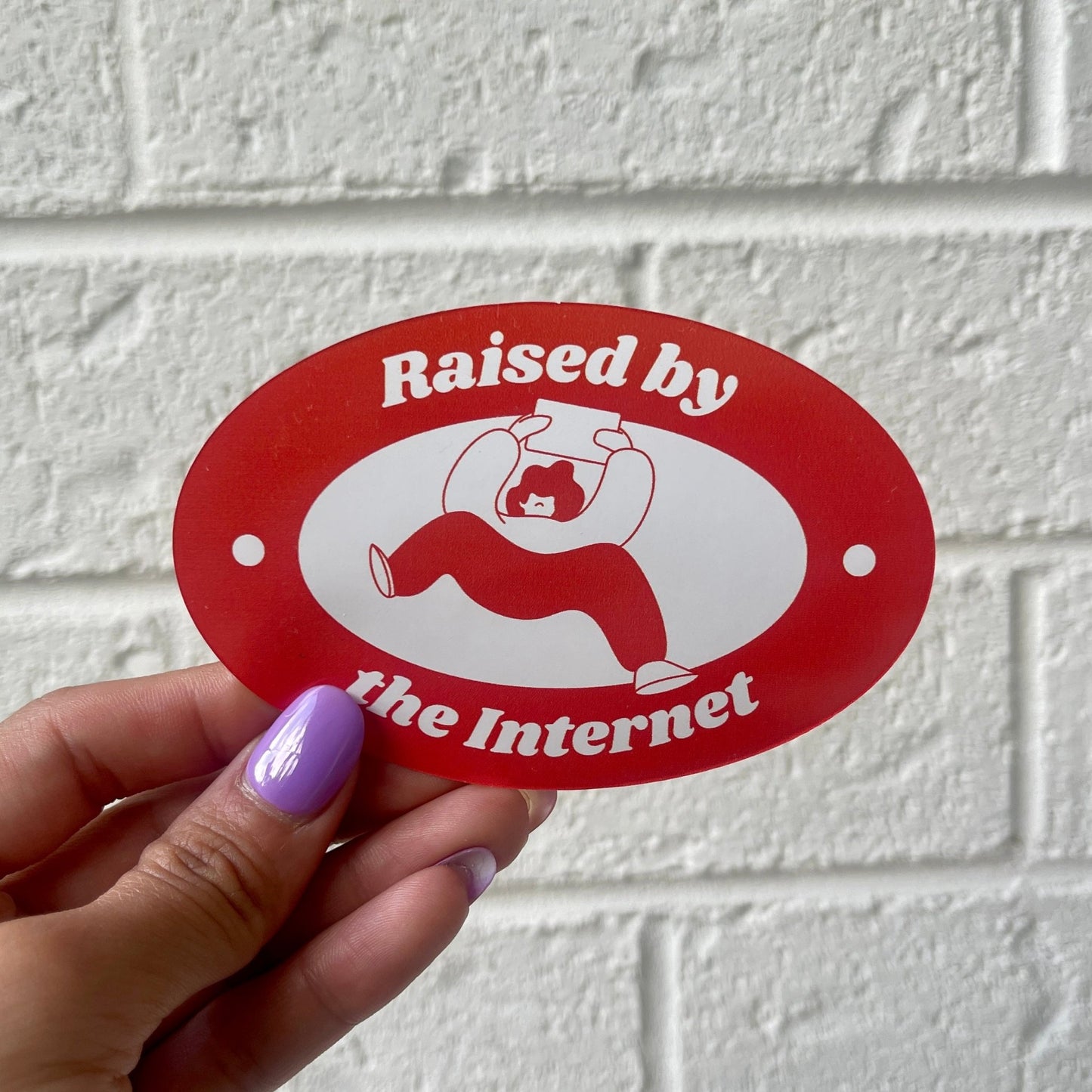 Oval sticker with a red background featuring the text 'Raised by the Internet' in white, along with an illustration of a person holding a tablet.