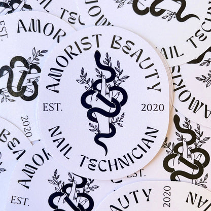 Oval stickers with the text 'Amorist Beauty Nail Technician EST. 2020' and an illustration of a hand holding a branch intertwined with a snake.