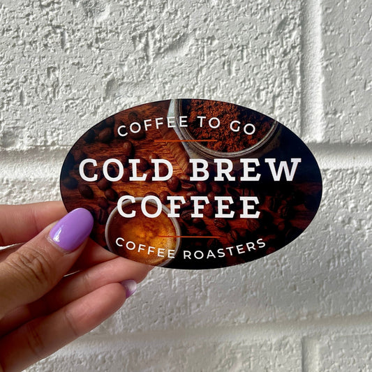 Oval sticker with a background of coffee beans and two coffee cups, featuring the text 'COFFEE TO GO COLD BREW COFFEE COFFEE ROASTERS' in white letters.