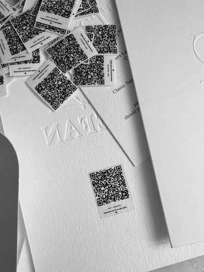 Clear Rectangle stickers featuring QR codes scattered on a white surface, some affixed to a paper with embossed text.